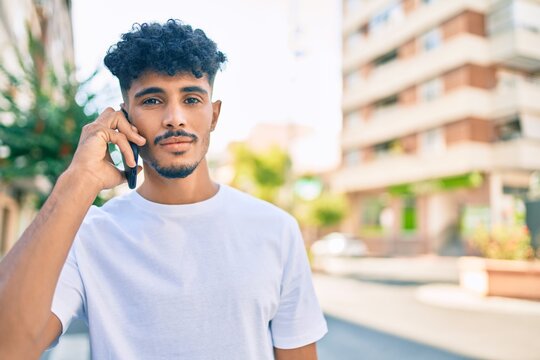 Young arab man with serious expression talking on the smartphone walking at city.