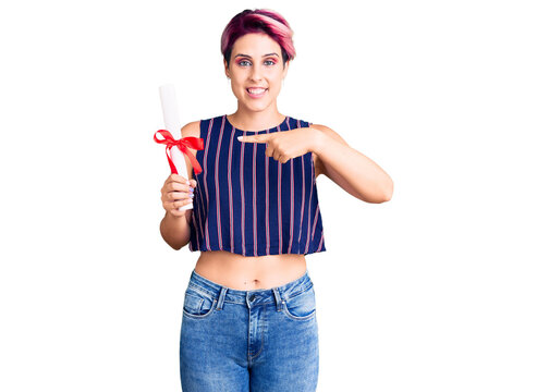 Young beautiful woman with pink hair holding graduate degree diploma smiling happy pointing with hand and finger