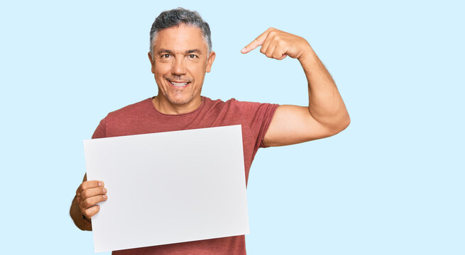Handsome middle age man holding blank empty banner pointing finger to one self smiling happy and proud