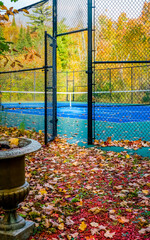 Tennis court under autumn blue sky, leaves changing colors, gate to court open