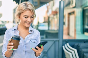 Young blonde woman smiling happy using smartphone and drinking take away coffee at the city.