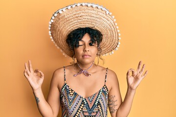 Young hispanic woman holding mexican hat relax and smiling with eyes closed doing meditation gesture with fingers. yoga concept.