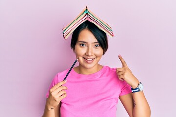 Beautiful young woman with short hair holding book over head smiling happy pointing with hand and...