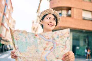 Young latin tourist girl on vacation smiling happy holding map at the city.