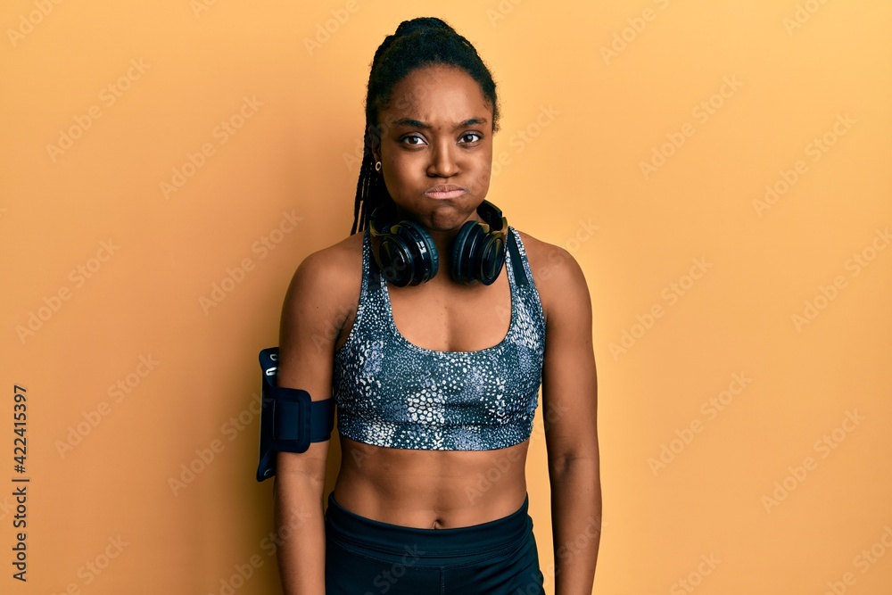 Poster african american woman with braided hair wearing sportswear and arm band puffing cheeks with funny f