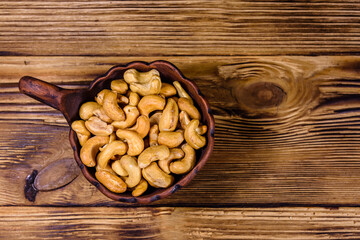 Ceramic bowl with roasted cashew nuts on a wooden table. Top view