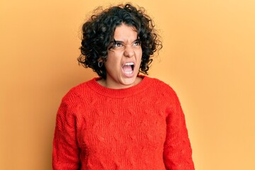 Obraz na płótnie Canvas Young hispanic woman with curly hair wearing casual winter sweater angry and mad screaming frustrated and furious, shouting with anger. rage and aggressive concept.
