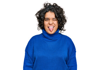 Young hispanic woman with curly hair wearing turtleneck sweater sticking tongue out happy with funny expression. emotion concept.