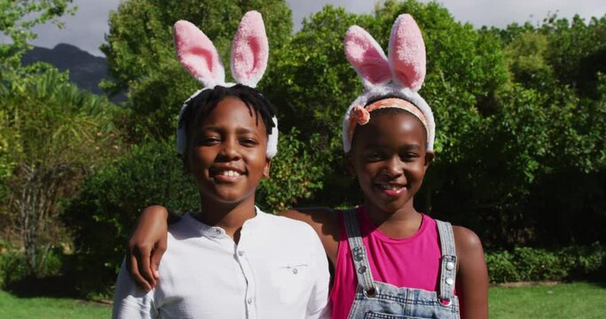 Smiling african american brother and sister wearing easter bunny ears embracing in garden