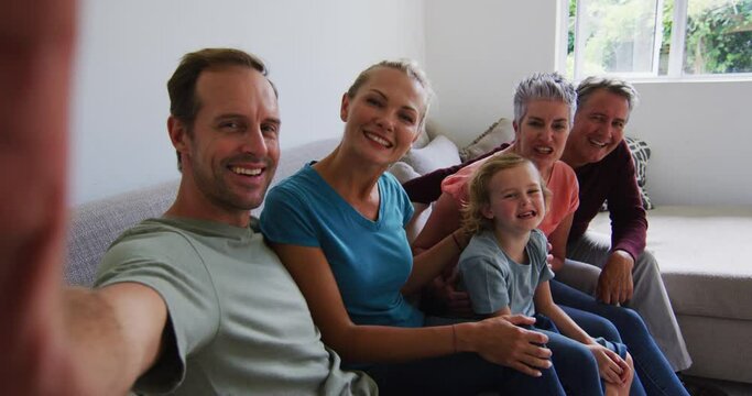 Caucasian parents, grandparents and grandchildren taking selfie sitting on couch smiling