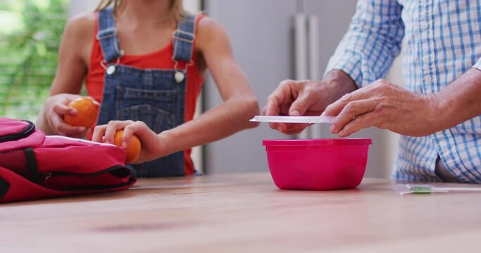 Midsection of caucasian grandfather in kitchen preparing packed lunch with granddaughter