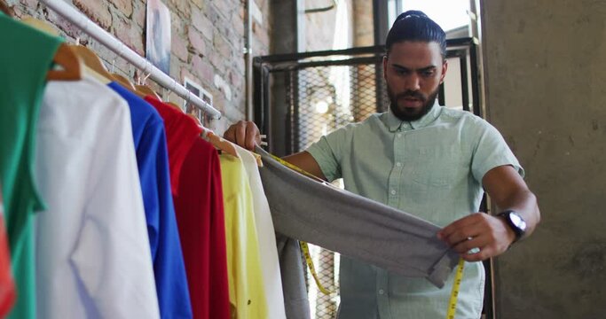Mixed race male fashion designer looking at different clothes and smiling