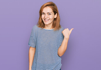 Young caucasian woman wearing casual clothes smiling with happy face looking and pointing to the side with thumb up.