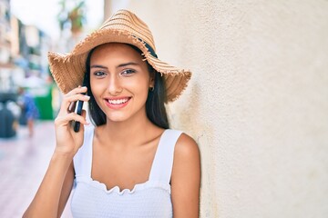 Young latin girl wearing summer style talking on the smartphone leaning on the wall.