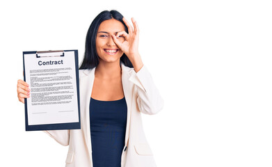 Fototapeta premium Young beautiful latin girl holding clipboard with contract document smiling happy doing ok sign with hand on eye looking through fingers