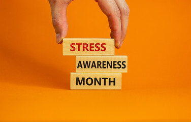 Stress awareness month symbol. Wooden blocks with words 'Stress awareness month'. Beautiful orange background. Doctor hand. Psychological, business and stress awareness month concept. Copy space.