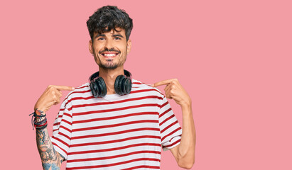 Young hispanic man listening to music using headphones looking confident with smile on face, pointing oneself with fingers proud and happy.