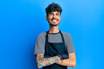Young hispanic man wearing barber apron happy face smiling with crossed arms looking at the camera....