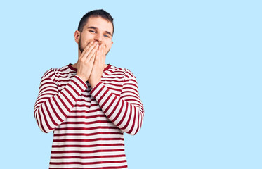 Young handsome man wearing striped sweater laughing and embarrassed giggle covering mouth with...