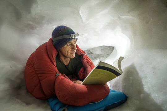 A Man Reading Before Bed By Headlamp In A Snowcave, San Juan Mountains, Silverton, Colorado.