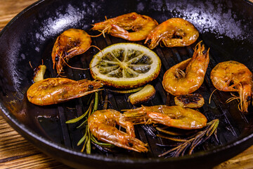 Roasted shrimps with lemon slice, garlic and rosemary in a cast iron pan