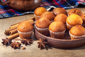 Small chocolate muffins in a ceramic plate on a wooden table. Composition of fresh pastries with cinnamon sticks and star anise. Fresh bakery.