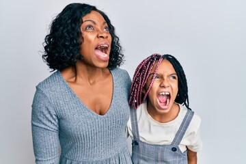 Beautiful african american mother and daughter wearing casual clothes and hugging angry and mad screaming frustrated and furious, shouting with anger. rage and aggressive concept.