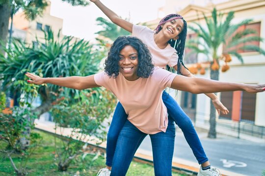 Beautiful african american mother giving daughter piggyback ride with open arms at the park.