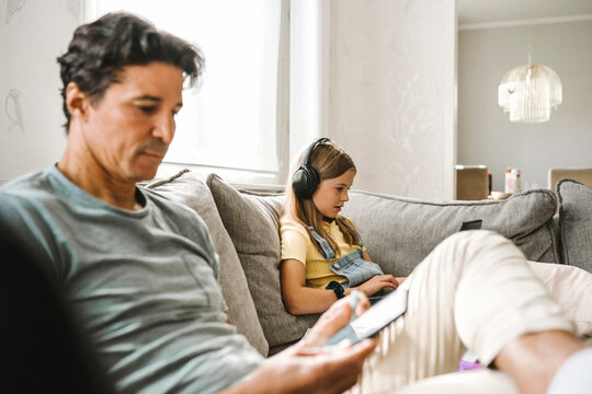 Father using smart phone while daughter e-learning through laptop in living room