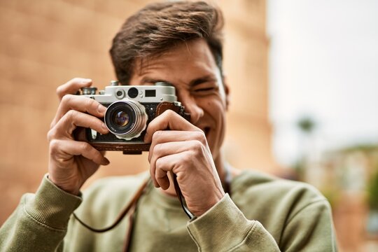 Young hispanic tourist man smiling happy using vintage camera at the city.