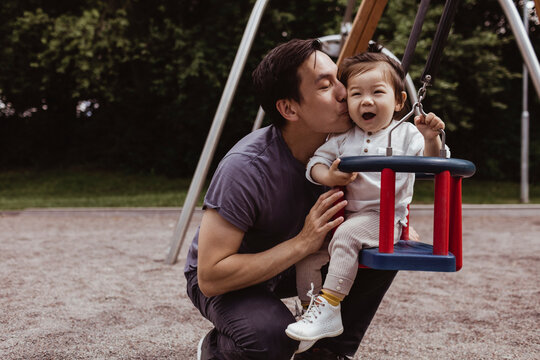 Smiling father kissing son while sitting on swing in playground