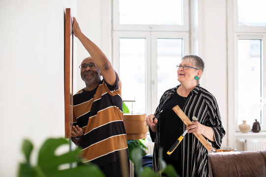 Smiling senior couple hanging painting on wall at home