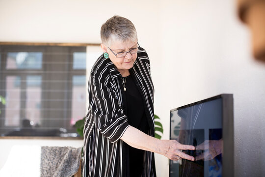 Senior woman touching television screen in living room