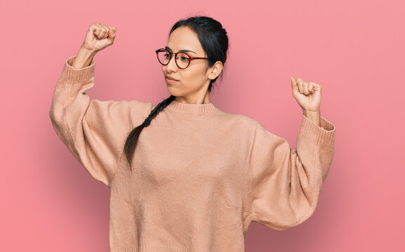Young hispanic girl wearing casual clothes and glasses showing arms muscles smiling proud. fitness concept.