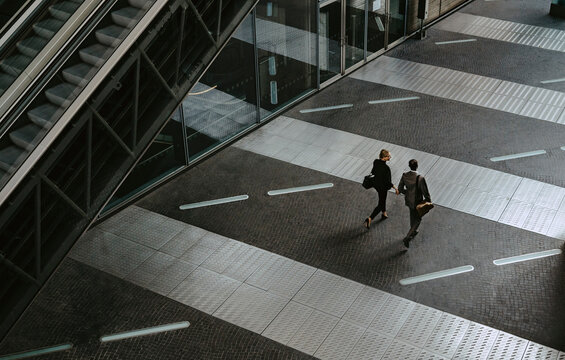 Rear view of male and female colleagues walking by escalator on walkway