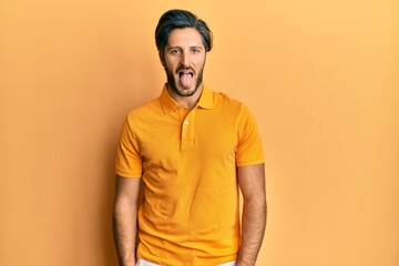 Young hispanic man wearing casual yellow t shirt sticking tongue out happy with funny expression. emotion concept.