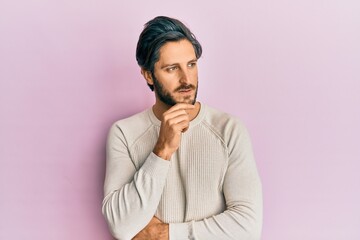Young hispanic man wearing casual winter sweater with hand on chin thinking about question, pensive expression. smiling with thoughtful face. doubt concept.