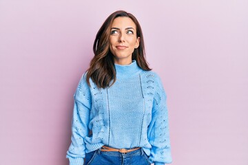 Young brunette woman wearing casual winter sweater over pink background smiling looking to the side...