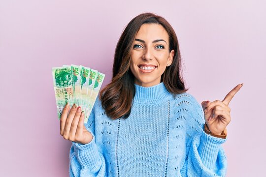 Young brunette woman holding hong kong 50 dollars banknotes smiling happy pointing with hand and finger to the side