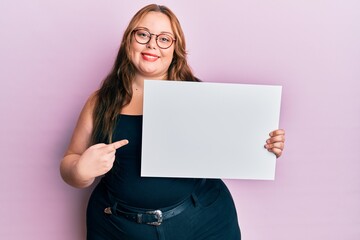 Naklejka premium Plus size caucasian young woman holding blank empty banner smiling happy pointing with hand and finger