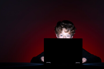 Boy with computer surfing internet alone on dark background