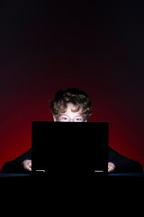 Boy with computer surfing internet alone on dark background