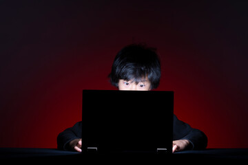Asian boy with computer surfing internet alone on dark background