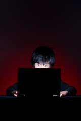 Asian boy with computer surfing internet alone on dark background