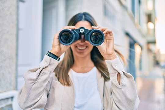 Young caucasian woman smiling happy looking for new opportunity using binoculars walking at the city.