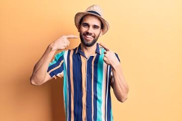 Young handsome man with beard wearing summer hat and shirt smiling cheerful showing and pointing with fingers teeth and mouth. dental health concept.