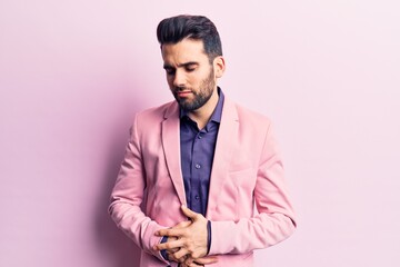 Young handsome man with beard wearing elegant jacket with hand on stomach because indigestion, painful illness feeling unwell. ache concept.