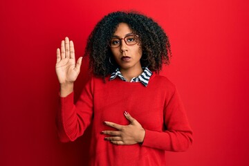 Beautiful african american woman with afro hair wearing sweater and glasses swearing with hand on...