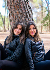 Naklejka premium Jóvenes gemelas posando junto a un árbol en mitad del campo. 
