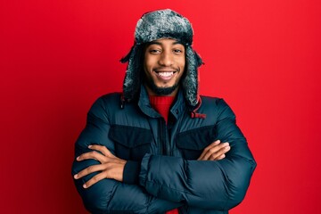 Young african american man with beard wearing winter hat and coat happy face smiling with crossed arms looking at the camera. positive person.